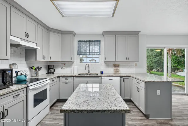 a kitchen with granite countertop sink stove and white cabinets
