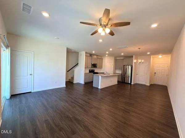 a view of an empty room with wooden floor and a kitchen