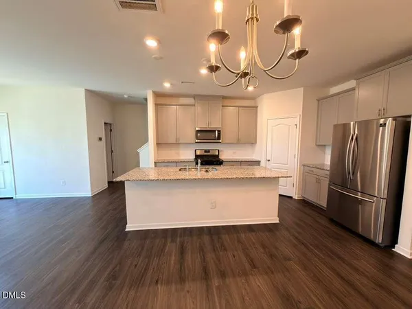 a large kitchen with stainless steel appliances a large counter top a wooden floor and a refrigerator