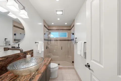 a bathroom with a granite countertop sink a toilet a mirror and shower