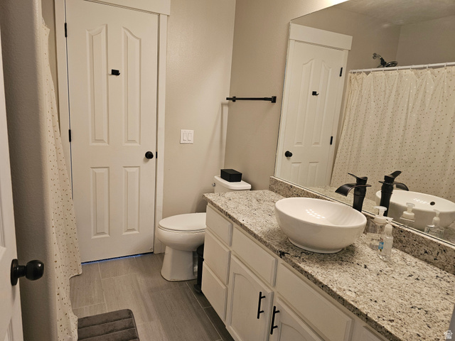 7481 Red Pine Road Eagle Mountain, UT 84005 - Photo 18 of 38 Upstairs hall bathroom featuring a white vessel sink, a speckled countertop, matte black fixtures, white cabinetry, and wood-finish tile flooring