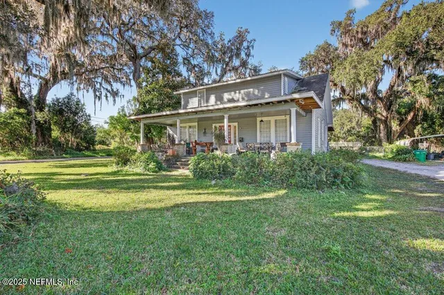 a view of a house with a big yard potted plants and large tree