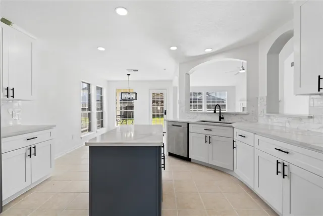 a large kitchen with granite countertop a sink white cabinets and stainless steel appliances