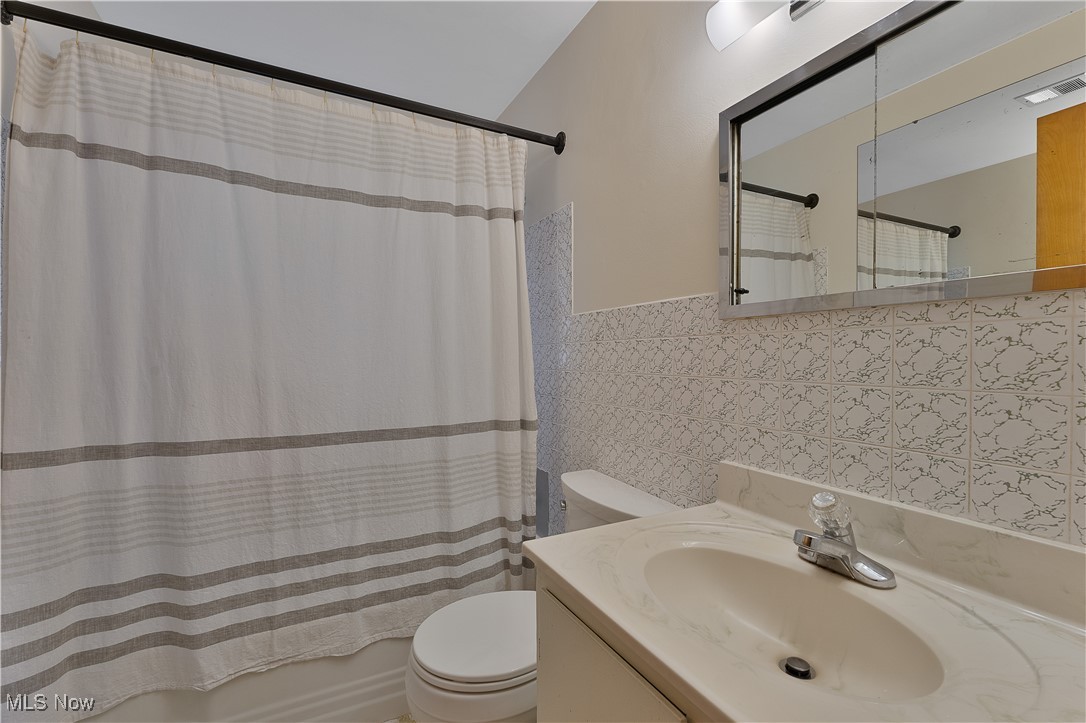 2702 Brunswick Road Youngstown, OH 44511 - Photo 15 of 18 Full bathroom featuring a wainscoted wall, shower / tub combo with curtain, tile walls, toilet, and vanity