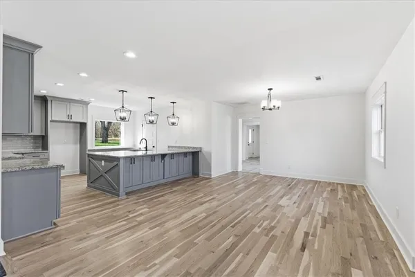 a large kitchen with kitchen island a sink dishwasher a refrigerator and white cabinets with wooden floor