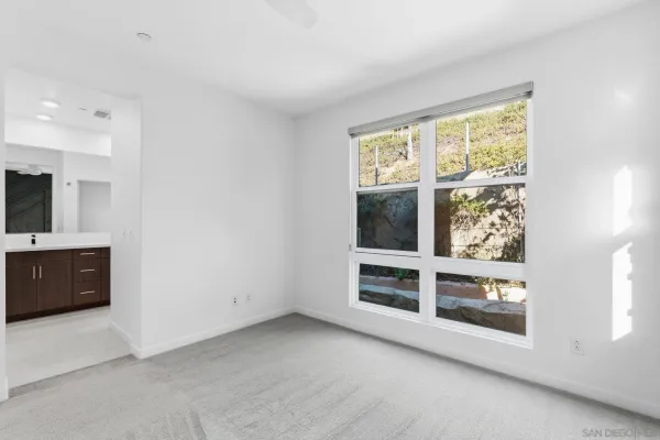 a view of an empty room with a window and kitchen view