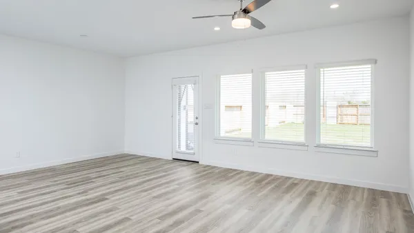 an empty room with wooden floor windows and fan