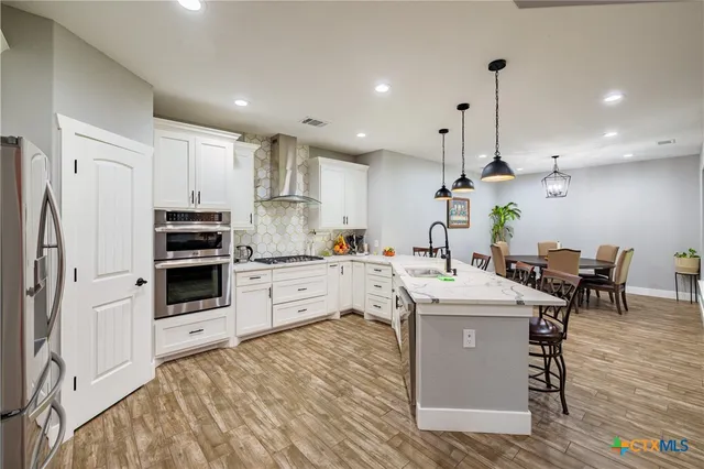 a kitchen with stainless steel appliances kitchen island granite countertop a stove a sink a refrigerator and white cabinets with wooden floor