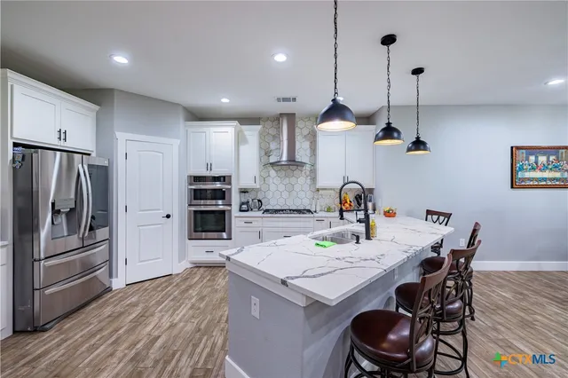 a kitchen with granite countertop kitchen island stainless steel appliances a stove a sink a refrigerator cabinets and wooden floor