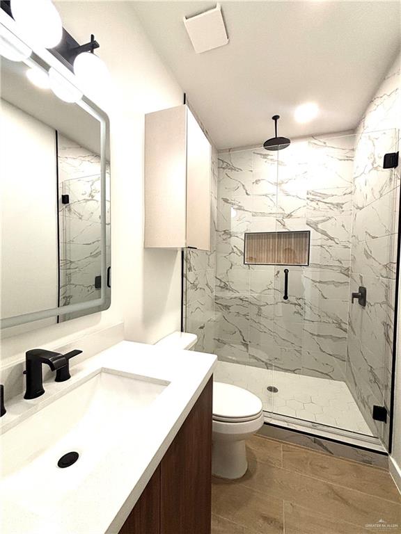 4 Estevan Street Mission, TX 78573 - Photo 16 of 24 Modern bathroom featuring a wood-finish vanity with an integrated white sink, matte black hardware, and a framed mirror with integrated lighting