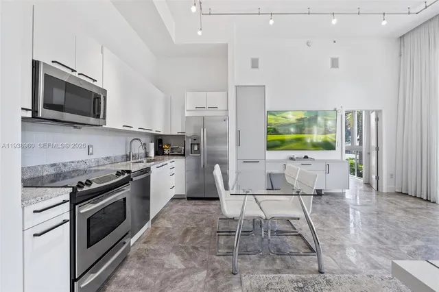 a kitchen with stainless steel appliances kitchen island granite countertop a stove a sink dishwasher a refrigerator a microwave oven with white cabinets and wooden floor