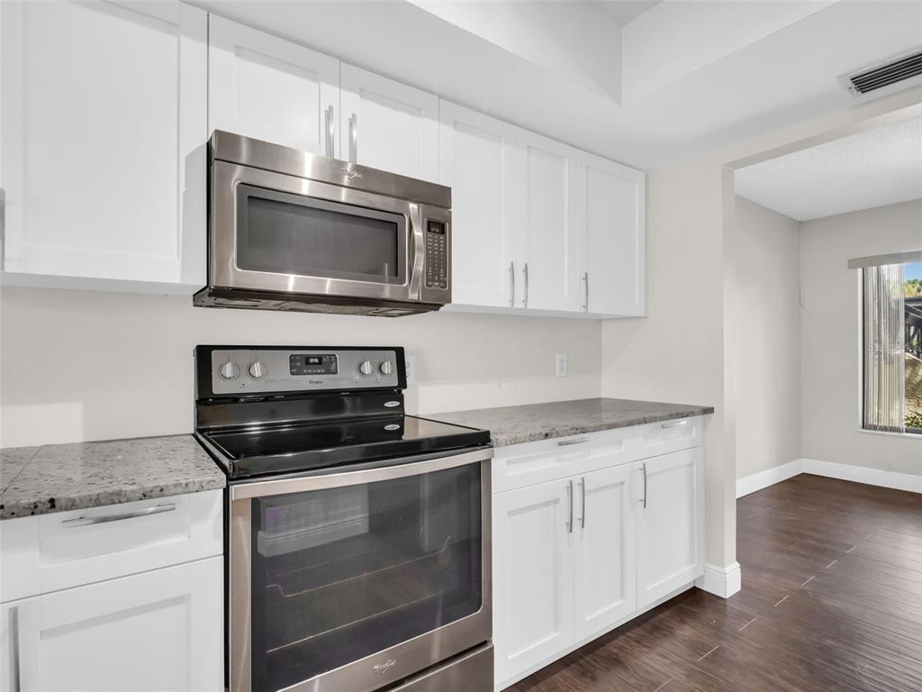 1801 East Lake Road South, Unit 20C Palm Harbor, FL 34685 - Photo 14 of 56 a kitchen with granite countertop white cabinets appliances and wooden floor