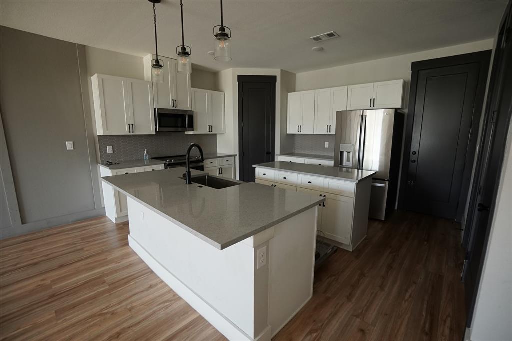 1764 Palladio Loop Princeton, TX 75407 - Photo 6 of 40 Modern kitchen featuring a central island with a sink, white cabinetry, stainless steel appliances, and wood-finish flooring