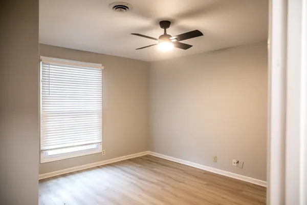 an empty room with wooden floor fan and windows