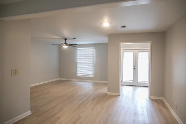 an empty room with wooden floor ceiling fan and windows