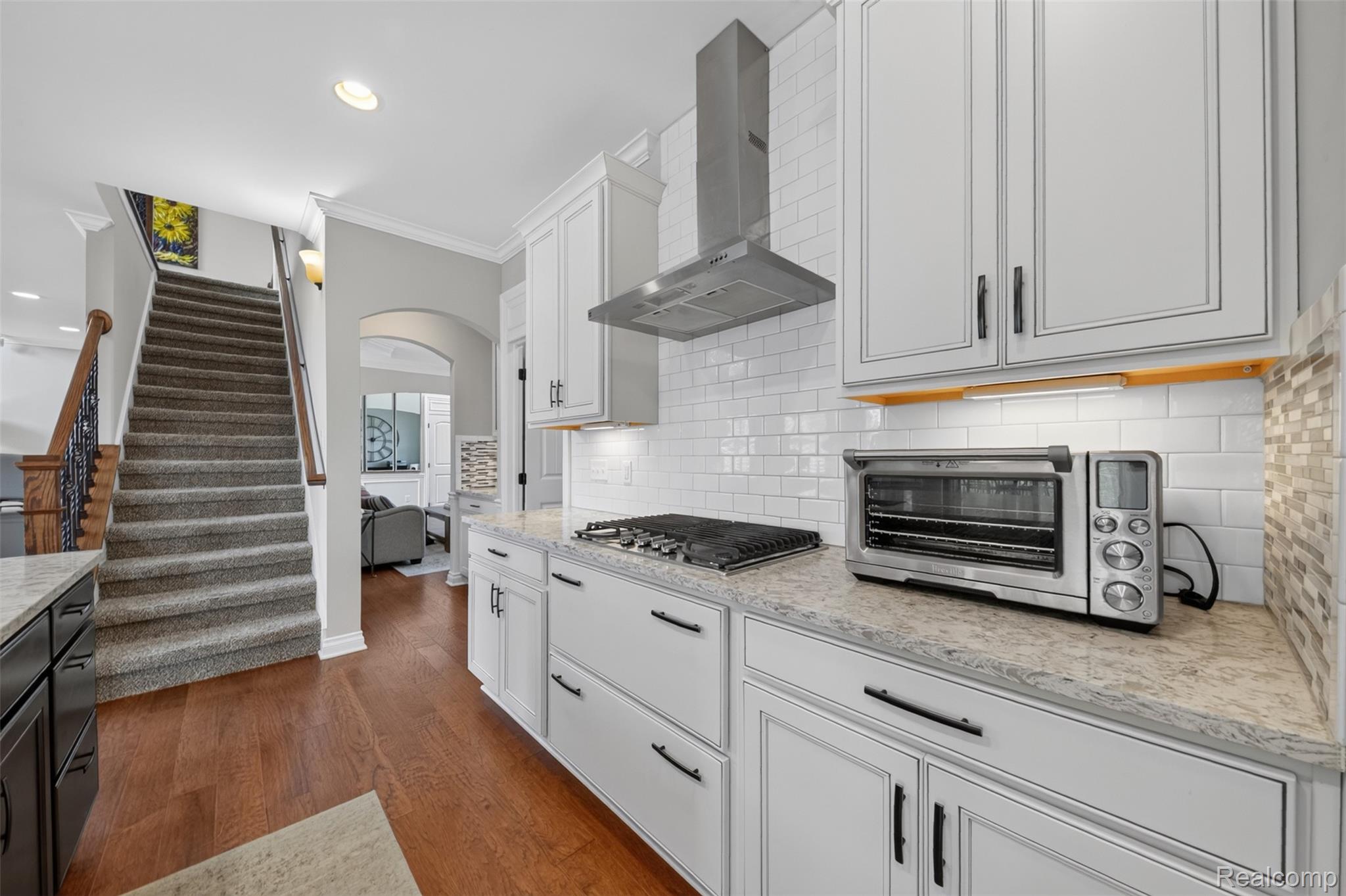 2531 Walnut View Drive Howell, MI 48855 - Photo 15 of 34 Kitchen featuring white shaker-style cabinetry, a white subway tile backsplash, light-toned countertops, a stainless steel range hood, and wood-finish flooring