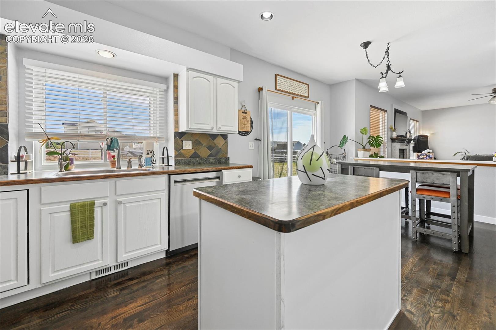 8347 Tibbs Road Peyton, CO 80831 - Photo 23 of 38 Kitchen featuring white cabinetry, dark wood-finish flooring, a central island with a dark countertop, and a tiled backsplash