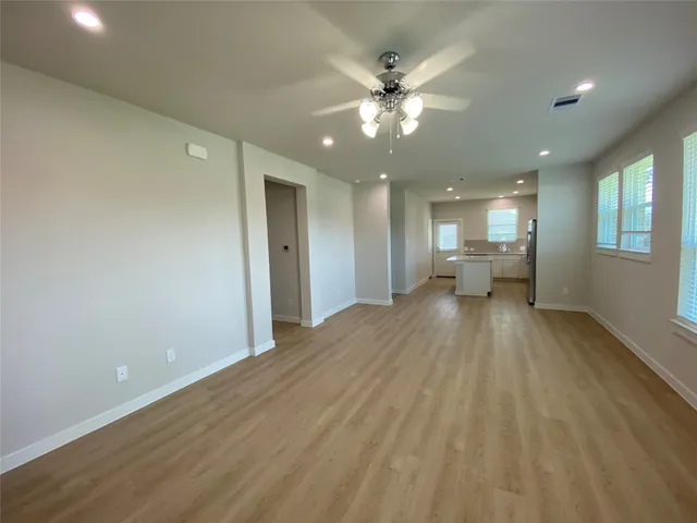 a view of a big room with wooden floor a ceiling fan and windows