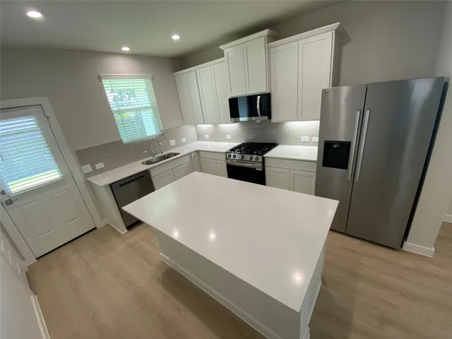 a large white kitchen with stainless steel appliances a refrigerator a stove a microwave a sink and white cabinets