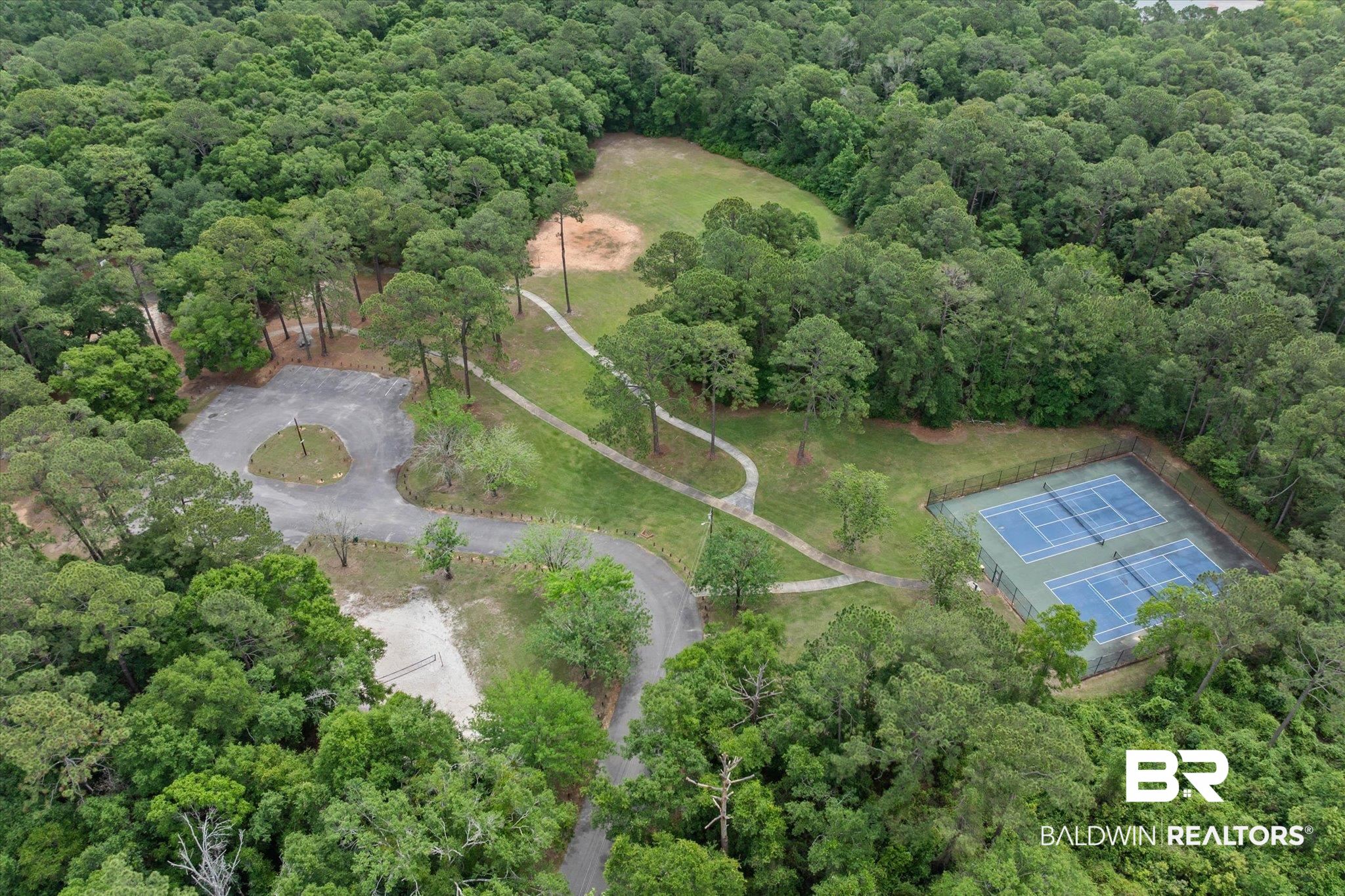 4213 Shan Drive East Mobile, AL 36693 - Photo 33 of 35 Aerial perspective of a verdant landscape featuring two fenced tennis courts with blue surfaces, a circular paved area, and meandering walking paths