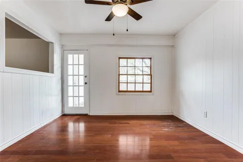 an empty room with wooden floor chandelier fan and windows