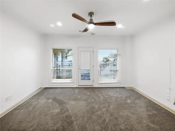 an empty room with chandelier fan and windows