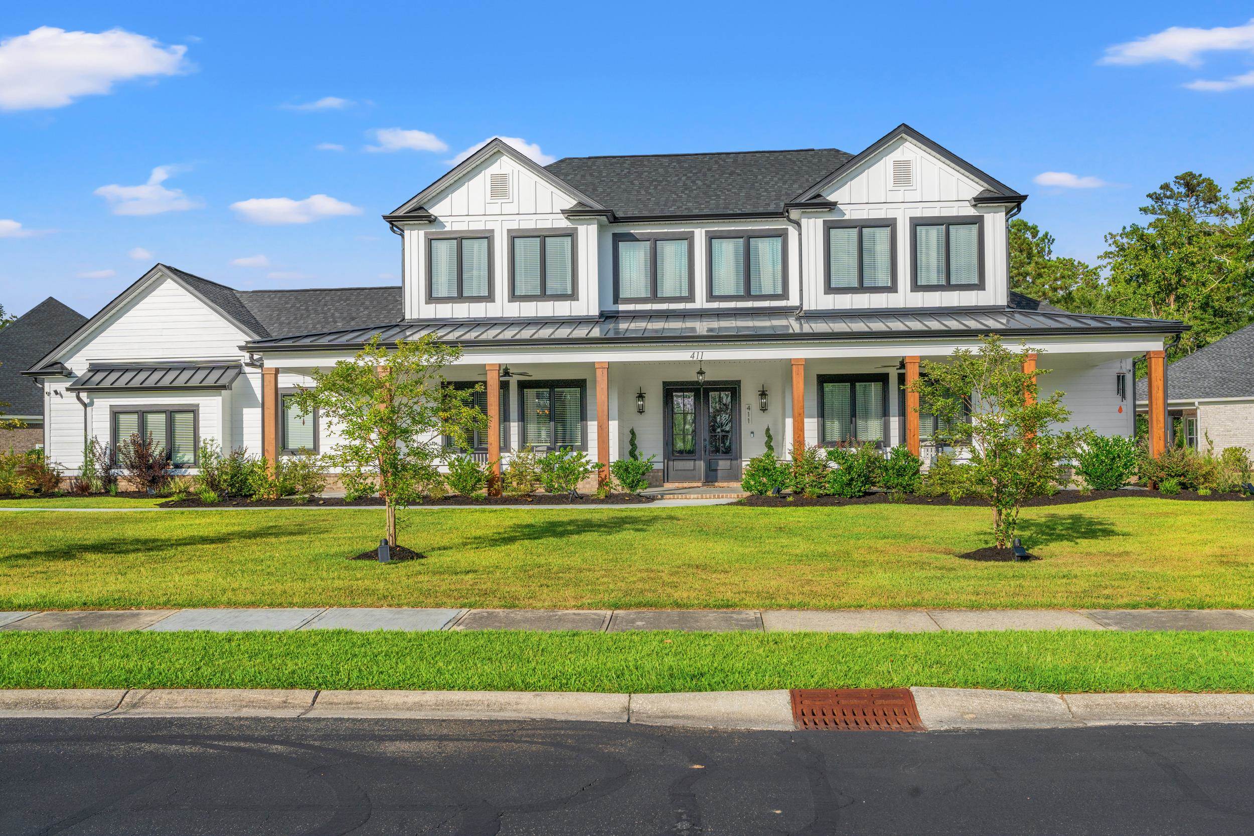 Modern farmhouse with a standing seam roof, covered porch, a front yard, and a metal roof