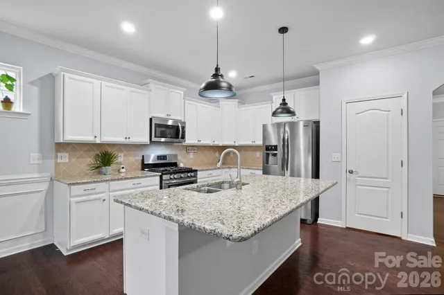 a kitchen with stainless steel appliances granite countertop a sink dishwasher a refrigerator white cabinets and wooden floor