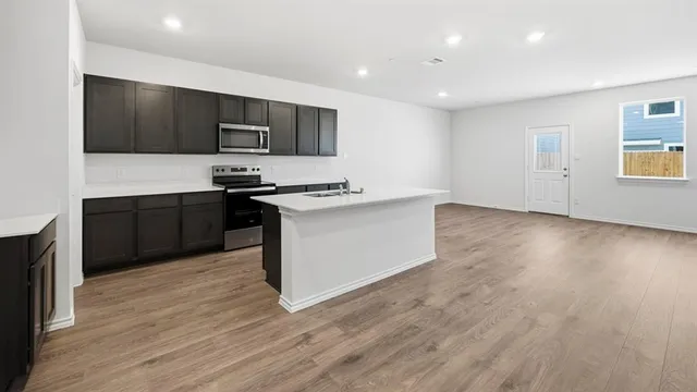 a kitchen with stainless steel appliances granite countertop a sink a stove a refrigerator cabinets and wooden floor