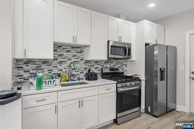 a kitchen with stainless steel appliances white cabinets and a stove a refrigerator a sink