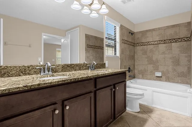 a bathroom with a granite countertop bathtub sink vanity mirror and toilet