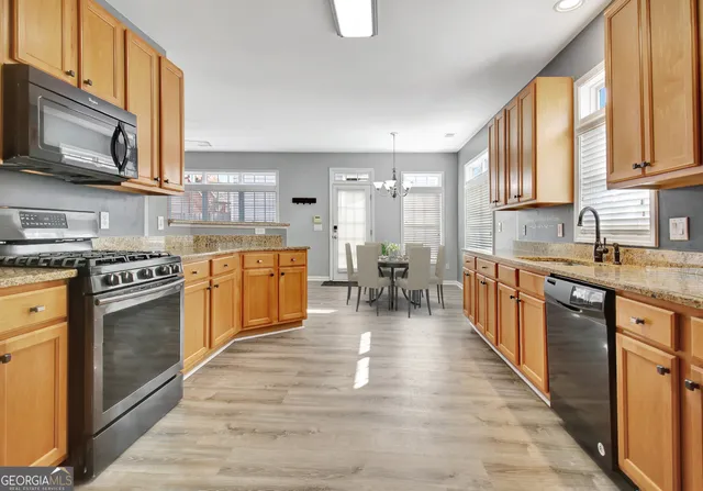 a large kitchen with stainless steel appliances granite countertop a stove top oven a sink dishwasher a dining table and chairs with wooden floor