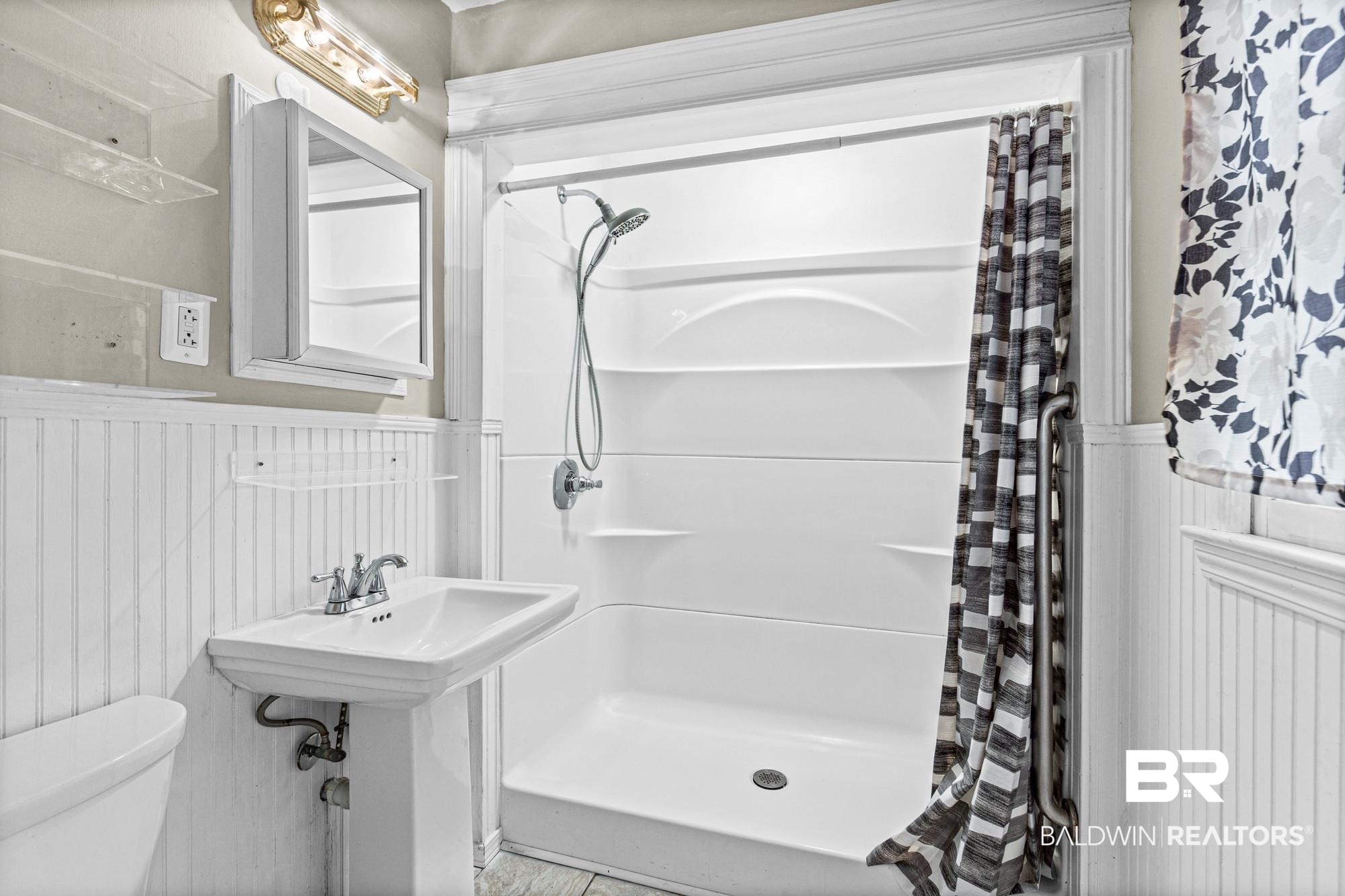 5510 Richmond Road Mobile, AL 36608 - Photo 9 of 21 White pedestal sink with chrome faucet, a white shower/tub combination with a chrome shower head, a medicine cabinet with mirror, and wainscoting paneling