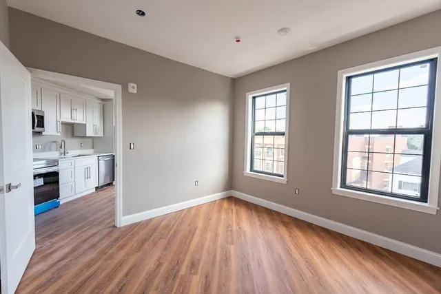 a view of a kitchen and an empty room with wooden floor and a window