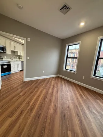 a view of an empty room with kitchen and refrigerator