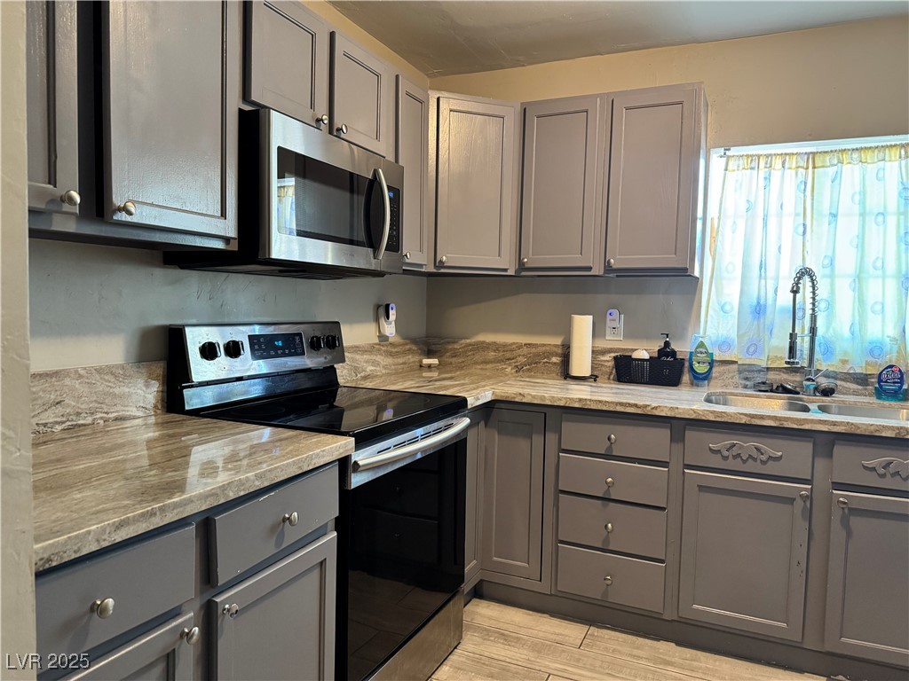 1409 Joshua Way Las Vegas, NV 89101 - Photo 2 of 15 Kitchen featuring gray cabinetry, appliances with stainless steel finishes, light wood-style floors, and light stone counters