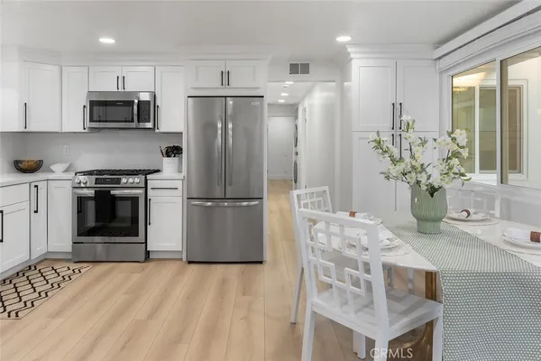 a kitchen with stainless steel appliances kitchen island granite countertop a refrigerator a stove a sink and white cabinets with wooden floor