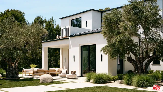 a view of a white house with a large tree and plants