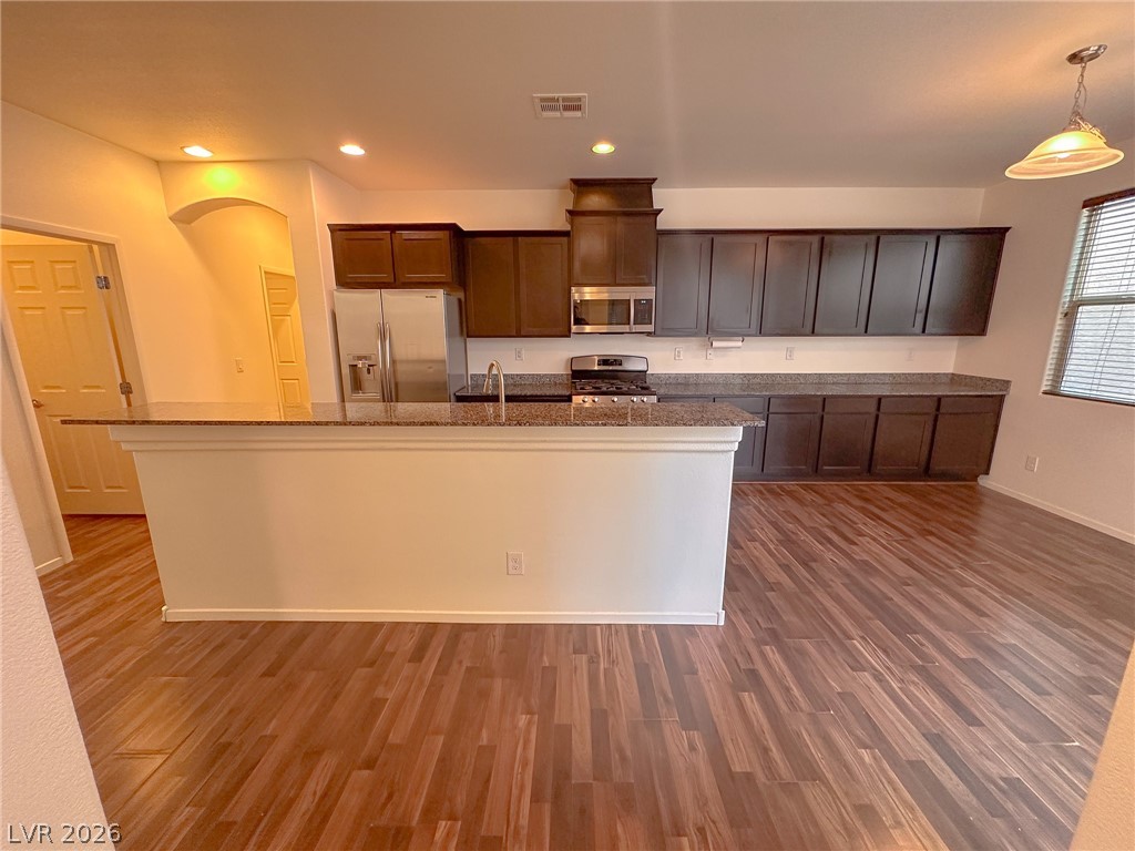 10934 Ketchikan Street Las Vegas, NV 89179 - Photo 25 of 30 Kitchen with stainless steel appliances, dark wood-style floors, dark stone counters, and an island with sink