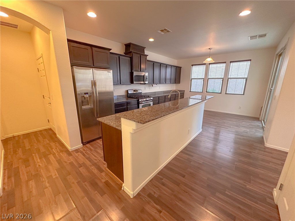 10934 Ketchikan Street Las Vegas, NV 89179 - Photo 26 of 30 Kitchen featuring stainless steel appliances, arched walkways, a kitchen island with sink, dark wood-type flooring, and light stone counters