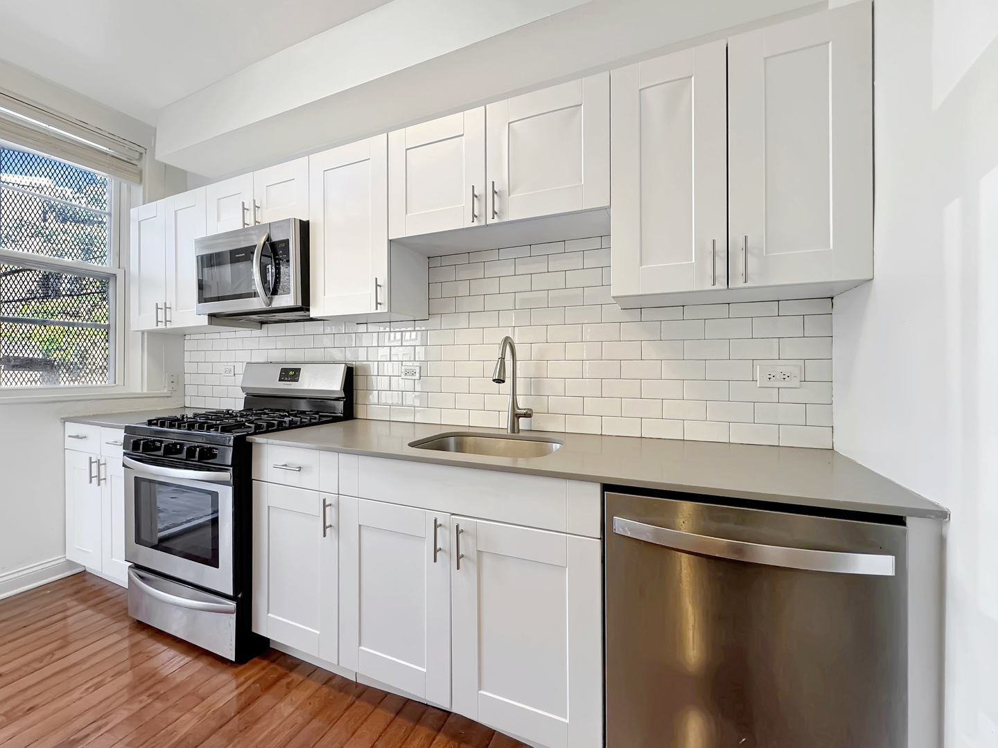 710 West Grace Street, Unit 2 Chicago, IL 60613 - Photo 5 of 12 a kitchen with stainless steel appliances granite countertop white cabinets a sink a stove a microwave and wooden floors