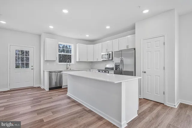 a kitchen with kitchen island a sink a stove a refrigerator and white cabinets with wooden floor