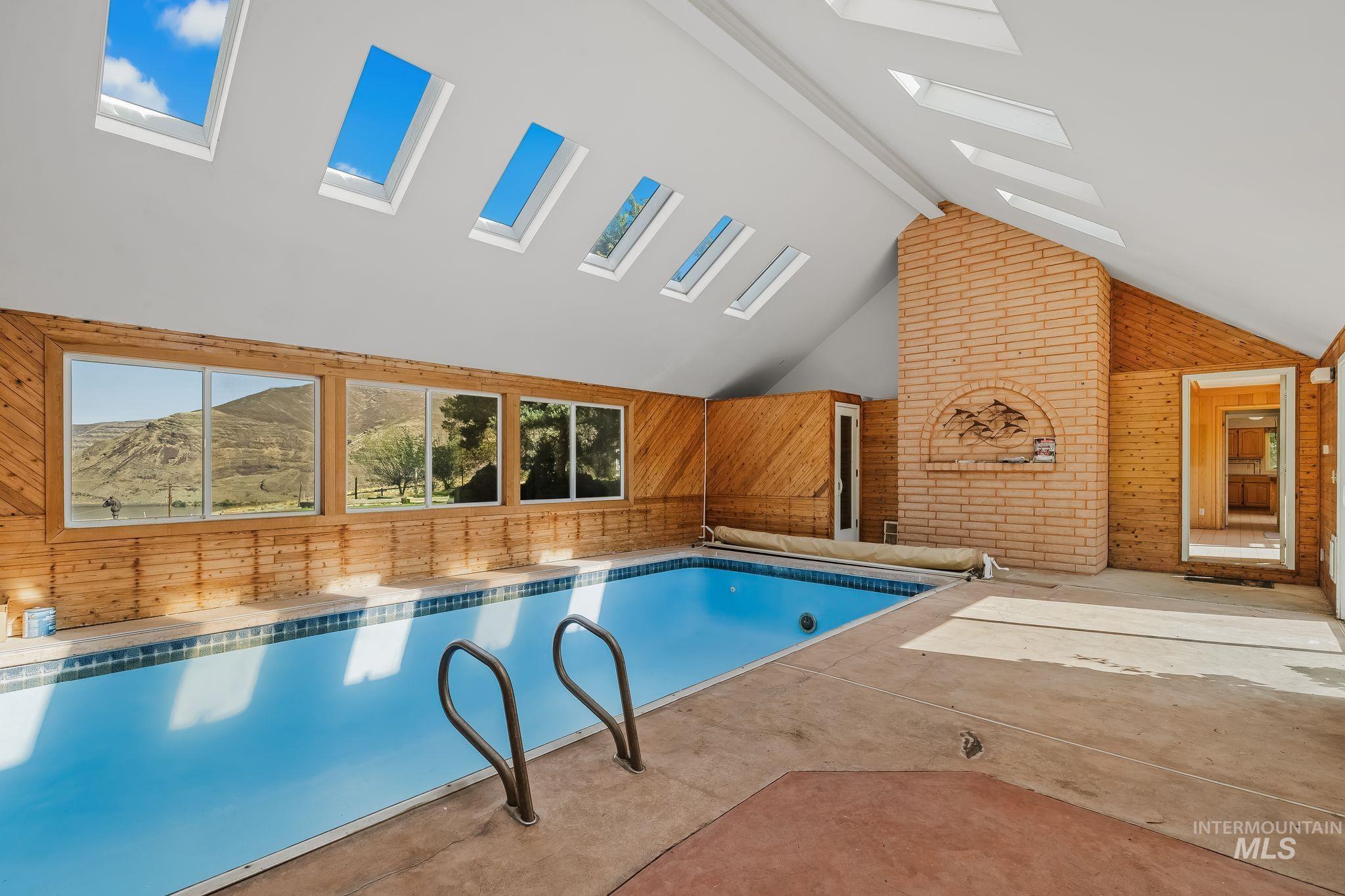 531 Silcott Road Clarkston, WA 99403 - Photo 6 of 43 Indoor swimming pool with integrated ladder, a brick-faced fireplace, multiple skylights, and extensive wood paneling