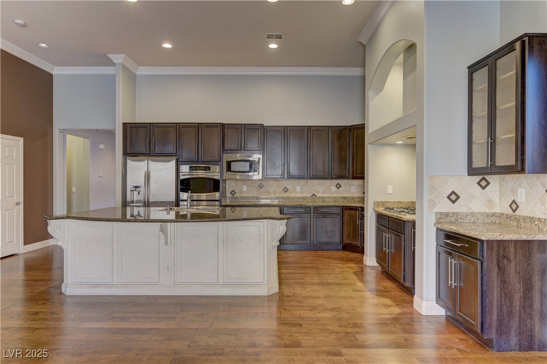 972 Rue Grand Paradis Lane Henderson, NV 89011 - Photo 8 of 32 Two tone kitchen featuring dark stone countertops, tasteful backsplash, stainless steel appliances, light wood-style floors, and crown molding