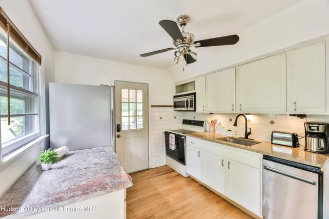 a kitchen with stainless steel appliances granite countertop a stove a sink dishwasher a refrigerator and white cabinets with wooden floor