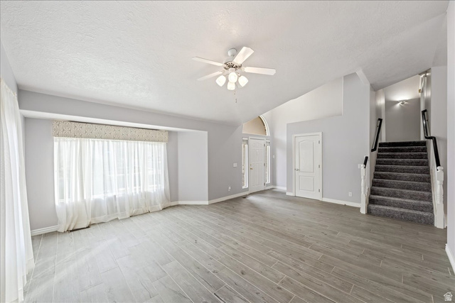 7 Reflection Way St. George, UT 84770 - Photo 7 of 54 Unfurnished living room with stairs, light wood finished floors, ceiling fan, lofted ceiling, and a textured ceiling