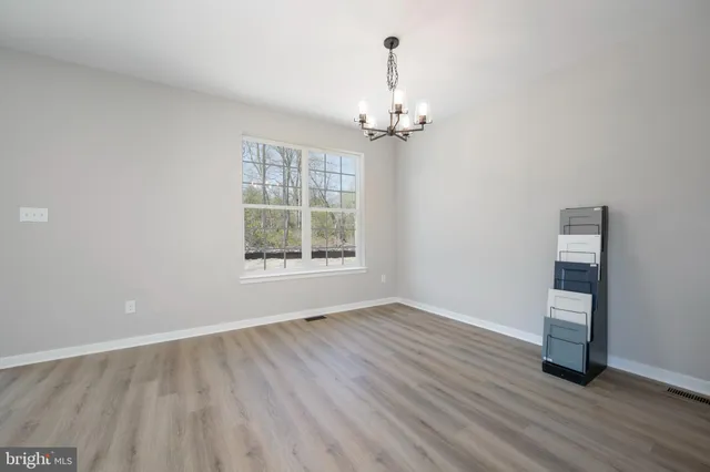 an empty room with wooden floor chandelier and windows