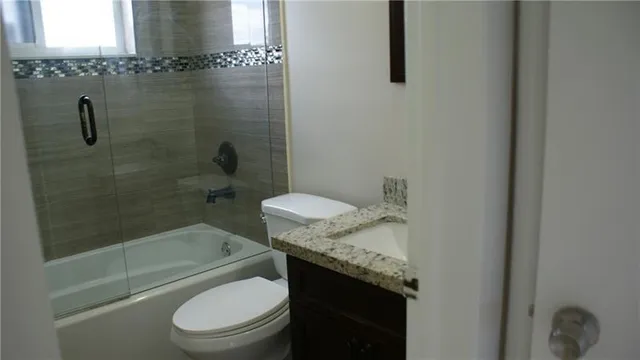 a bathroom with a granite countertop bathtub shower sink vanity and toilet