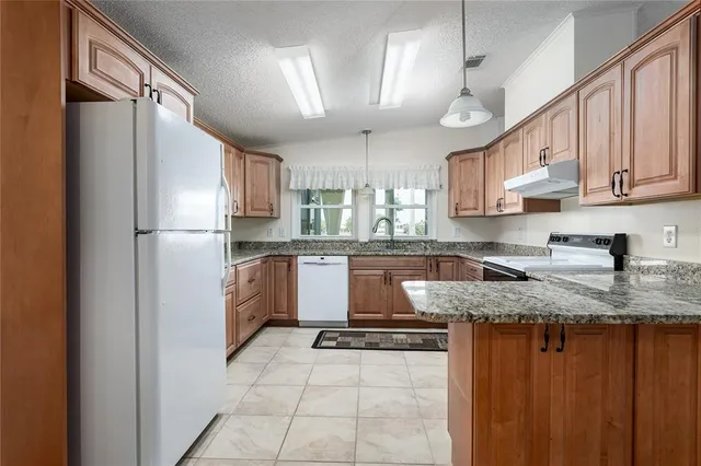 a kitchen with granite countertop a refrigerator a sink and white cabinets