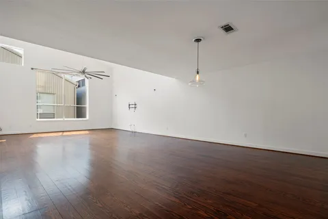 a view of an empty room with wooden floor and a ceiling fan